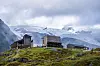 Moderne DNT-fjellhytter ved foten av en isbre under skyet himmel.