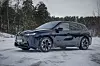 BMW iX parkert på snødekt underlag foran skog i vintervær. Med en lengde på neste fem meter og en høyde på 1,70 er BMW iX M70 xDrive en stor bil.