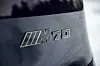 BMW M70-logo i nærbilde på mørk bil med vanndråper. Med denne logoen på hekken har du 659 hestekrefter og en voldsom akselerasjon tilgjengelig.
