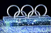 Opplyste olympiske ringer står på en isblokk under en seremoni i mørket.