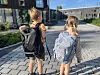 To barn med ryggsekker går på en steinlagt vei foran en skolebygning.