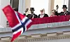 Kongefamilien vinker fra Slottsbalkongen bak et norsk flagg i forgrunnen.
