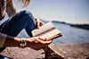 Person som sitter ute ved vannet og leser i en bok