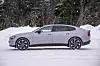 Lys Volvo ES90 sedan sett fra siden på snødekt vei foran skog. olvo ES90 er betydelig større enn Geely-fetteren Polestar 2, men fasongen er ikke ulik.