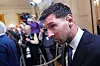 Lionel Messi i dress går forbi pressefotografer i et fullt presserom.