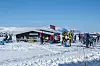Fjellkiosk omgitt av skiløpere på snødekt vidde med norske flagg og fjell i bakgrunnen.