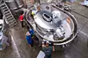 Teknikere arbeider rundt en stor, oval metalltank i et industriverksted.