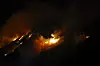 Lyngbrann i mørket med flammer og røyk som sprer seg oppover en åsside.