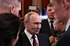 Putin står omgitt av flere personer i dress og uniform i en sal innendørs.