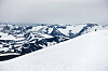 To skiløpere går over en snødekt fjellrygg med islagte topper i bakgrunnen.