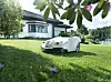 Hvit Husqvarna robotgressklipper kjører over grønn plen foran enebolig