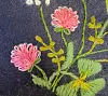 Et nærbilde av ferdig brodert motiv på mørkt stoff. Rosa blomster er laget med løkkesting som danner åpne løkker rundt kanten, kombinert med grønne blader og gule detaljer i andre stingtyper.