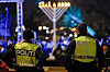 To politibetjenter med gule vester foran en opplyst hanukkah-lysestake utendørs om kvelden.