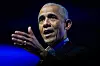 Barack Obama taler på en scene med blå bakgrunn og løftet hånd.