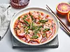 Tallerken med laks crudo i rød sitrussaus, toppet med chili, løk og grønne spirer. Tynne skiver rå laks i blodappelsinlake med chili, urter og spirer fremhever ren smak og frisk syre.