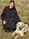 Kvinne sitter i tørt gress ved siden av lys labrador med førerhundsele