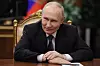 Vladimir Putin sitter ved et møtebord i Kreml med flagg i bakgrunnen.