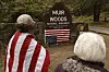 To personer ser mot Muir Woods-skilt med opp-ned amerikansk flagg hengt foran.