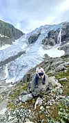 Person sitter på en stein foran en bratt norsk isbre i høyfjellet. Tureventyreren Johan Haugsrud utforsker norsk fjellnatur ved en isbreen Buarbreen, på jakt etter nye favoritturer å dele med følgerne sine.