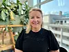 Kvinne i svart topp sitter foran vindu med planter og byutsikt bak