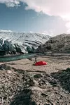 Rødt telt og en person står på gruslandskap ved foten av en isbre og elv. FRILUFTSLIV: En enslig turgåer med rødt telt camper ved isbreen Svelgabreen i Kvinnherad i Vestland fylke, og elv, på jakt etter nye norske naturopplevelser utenfor de mest kjente rutene.