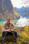 Smilende turgåer sitter på en stein med utsikt over fjord og høstfargede fjell.