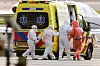 Helsepersonell i vernedrakter ledsager pasient inn i gul ambulanse ved flystripe