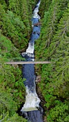 Luftfoto av en hengebro over et smalt juv med fossende elv omgitt av tett skog.