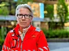 Person i rød redningsuniform står ute i et bymiljø med grønt i bakgrunnen
