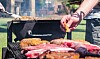 Nærbilde av kjøtt som grilles på utegrill med personer som snur maten.
