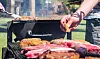 Nærbilde av kjøtt som grilles på utegrill med personer som snur maten.