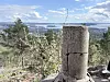 Sprekket betongstolpe foran skog og fjordutsikt i klart vær