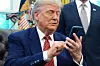 Donald Trump sitter ved skrivebordet i Det ovale kontor og betjener en smarttelefon.