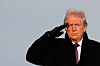 President som står utendørs og utfører en militær honnør mot lys himmel.