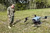 US Marine-soldat står ved siden av en TRV 150-drone på gressmark under øvelse