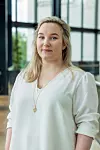 Kvinne i hvit bluse poserer innendørs foran store vinduer.