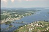Luftfoto av småby ved bred elv med bro og omgivende jordbrukslandskap