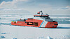 Rødt forskningsfartøy i sjøis foran fjerne snødekte fjell.