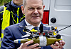 Olaf Scholz viser fram en liten militær dronekopi under et politibesøk utendørs