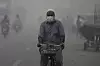 Mann med maske sykler gjennom tett smog på en vei i Lahore