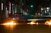 Blå veteranbil passerer flammende veisperring i mørklagt gate i Havana