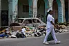 Sykepleier i hvit uniform går forbi søppel og utbrent bilvrak i en gate i Havana