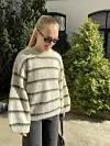 Bildet viser Ova Summer Sweater fra ByHollekim brukt utendørs i sommersol. Genseren har en oversized passform, brede ermer, rund hals og horisontale striper i et luftig mohairgarn. Den er stylet med mørke jeans, solbriller og liten veske, noe som gir et avslappet hverdagsuttrykk.