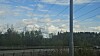 Kraftlinjer over vei ved skogkledd område under blå himmel