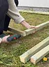 Hender som skrur sammen trykkimpregnerte bjelker på en gressplen med drill.