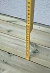 Tommestokk som måler høyden på terrassebord ved en husvegg.