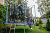 To personer leker på en trampoline i en grønn hage med blomster og trær.