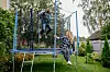 To personer leker på en trampoline i en grønn hage med blomster og trær.