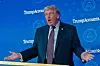 Donald Trump taler foran blå Trump Accounts-bakvegg i et auditorium