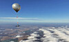 Sølvfarget ballong med instrumenter svever over skyer og åkre